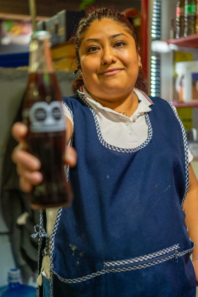 Friendly woman in Ciudad de México offering a soda bottle with a smile in a local supermarket.