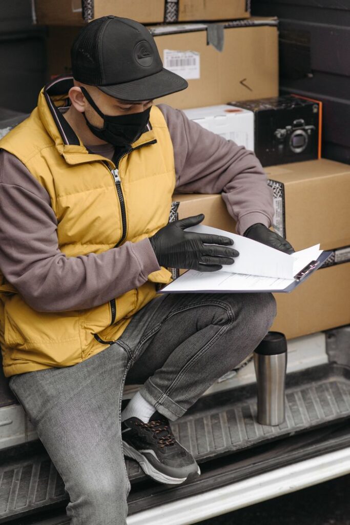 Delivery courier reviewing documents with packages in a van, adhering to safety protocols.